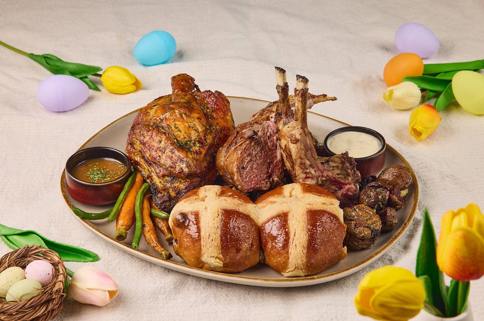Little Farms Easter platter with roasted lamb rack, roasted chicken, vegetables, potatoes, and sourdough hot cross buns.