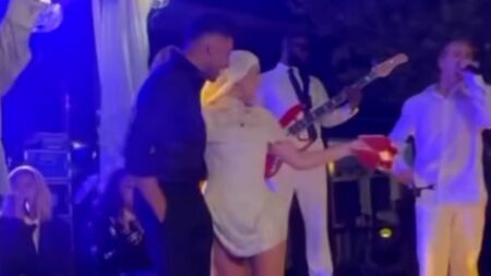 Perrie Edwards poses in her second wedding dress and a dramatic veil as she kicks off her bridal heels while being serenaded with remix of Marry You at wild party